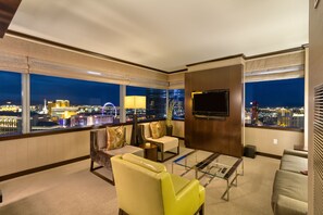 Enjoy a panoramic city view from the comfort of this stylish room, featuring a seating area with sofa and armchairs, flat-screen TV, and large windows.