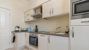 Ett kompakt kök med vita skåp, en inbyggd ugn, en mikrovågsugn och ett diskho.