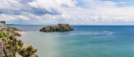 A coastal view with a rocky outcrop, clear skies, and calm sea.