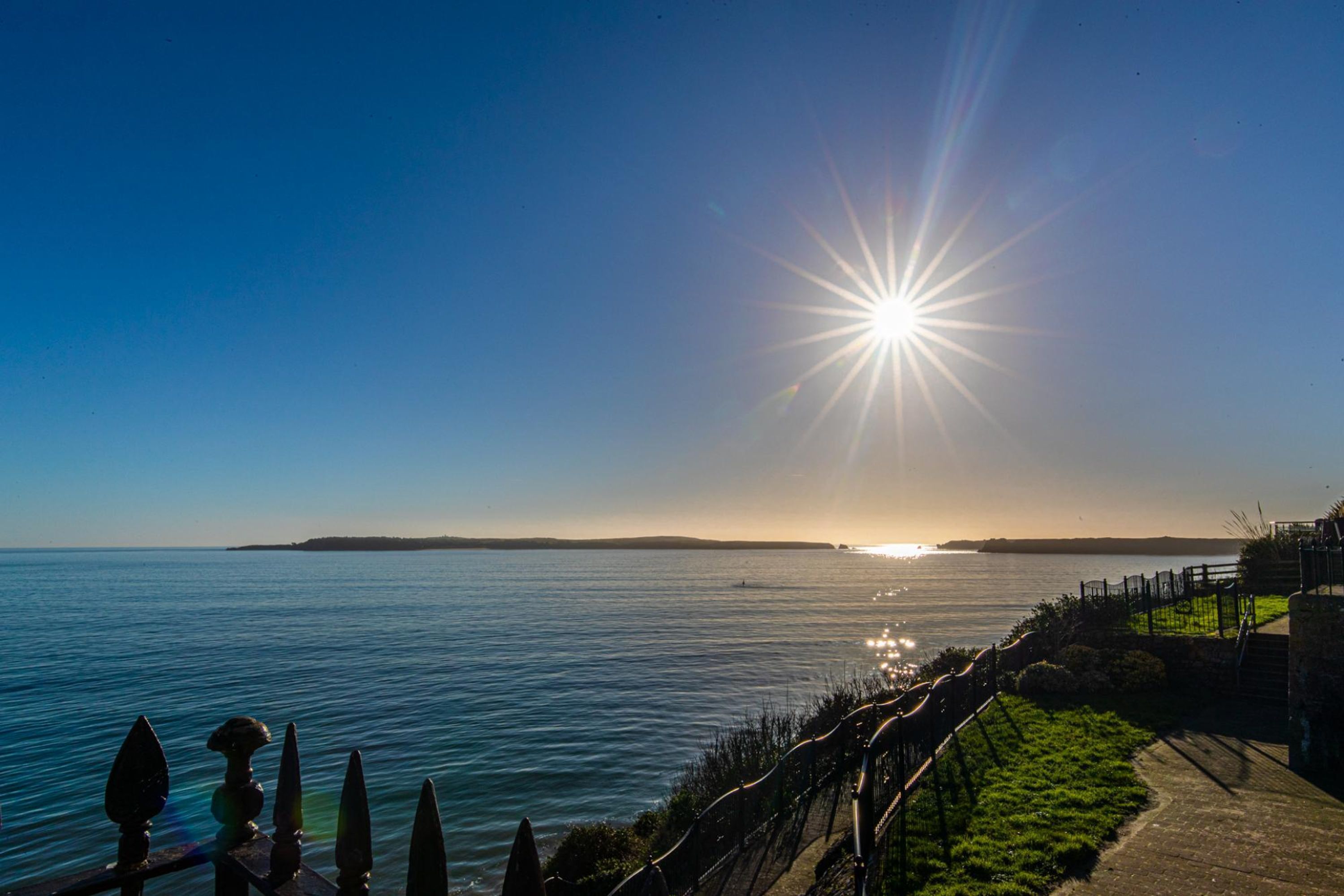 Une vue sur la côte, avec un ciel dégagé, un horizon illuminé par le soleil et un sentier longeant le bord de l’eau.