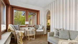 Ein gemütliches Wohnzimmer mit einer Couch, einem Sessel, einem kleinen Tisch und einem Fenster mit Blick ins Grüne.