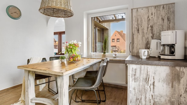 Eine Küche mit einem Holztisch, zwei Stühlen, einer Weidenleuchte und einer Kaffeemaschine, mit Blick auf umliegende Gebäude.