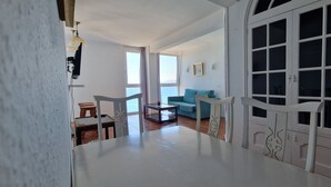 Un salón amplio con un sofá, una mesa de centro y una mesa de comedor. Se aprecia un ventanal con cortinas y vistas al exterior.