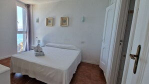 Habitación de hotel con cama, escritorio, silla, ventana con vistas y dos cuadros en la pared.