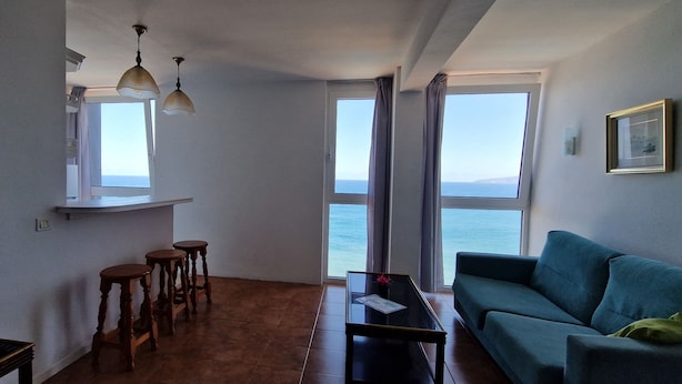 Una sala de estar con un sofá, una mesa de centro, un televisor y una ventana con vista al mar.