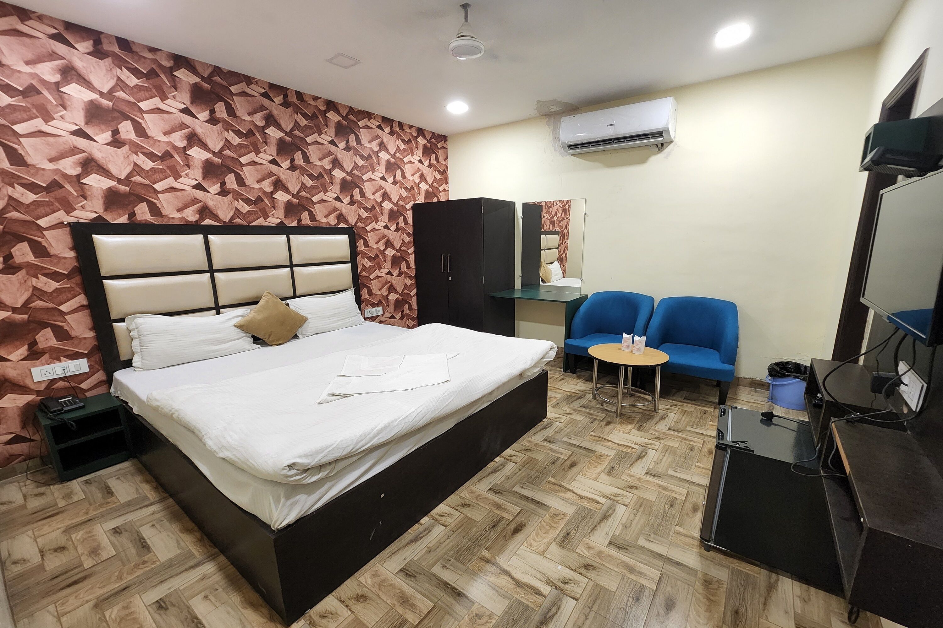 A hotel room with a bed, a wardrobe, a desk with a computer, a chair, and a small table.