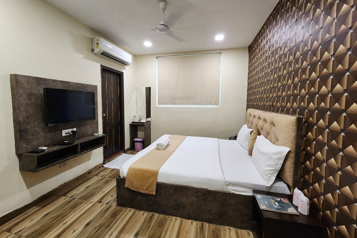 A bedroom with a bed, a television, a ceiling fan, and a window.