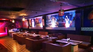 Een restaurant met weinig licht, voorzien van zitjes en tafels, een vloer met patroon en wandmontage schermen die beelden tonen.