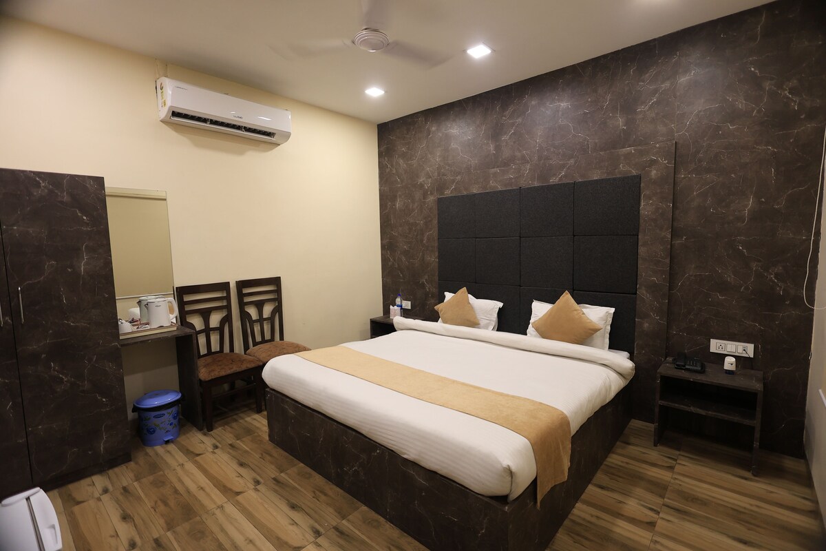 A hotel room with a large bed, a chest of drawers, a small table, and a wall-mounted air conditioner.