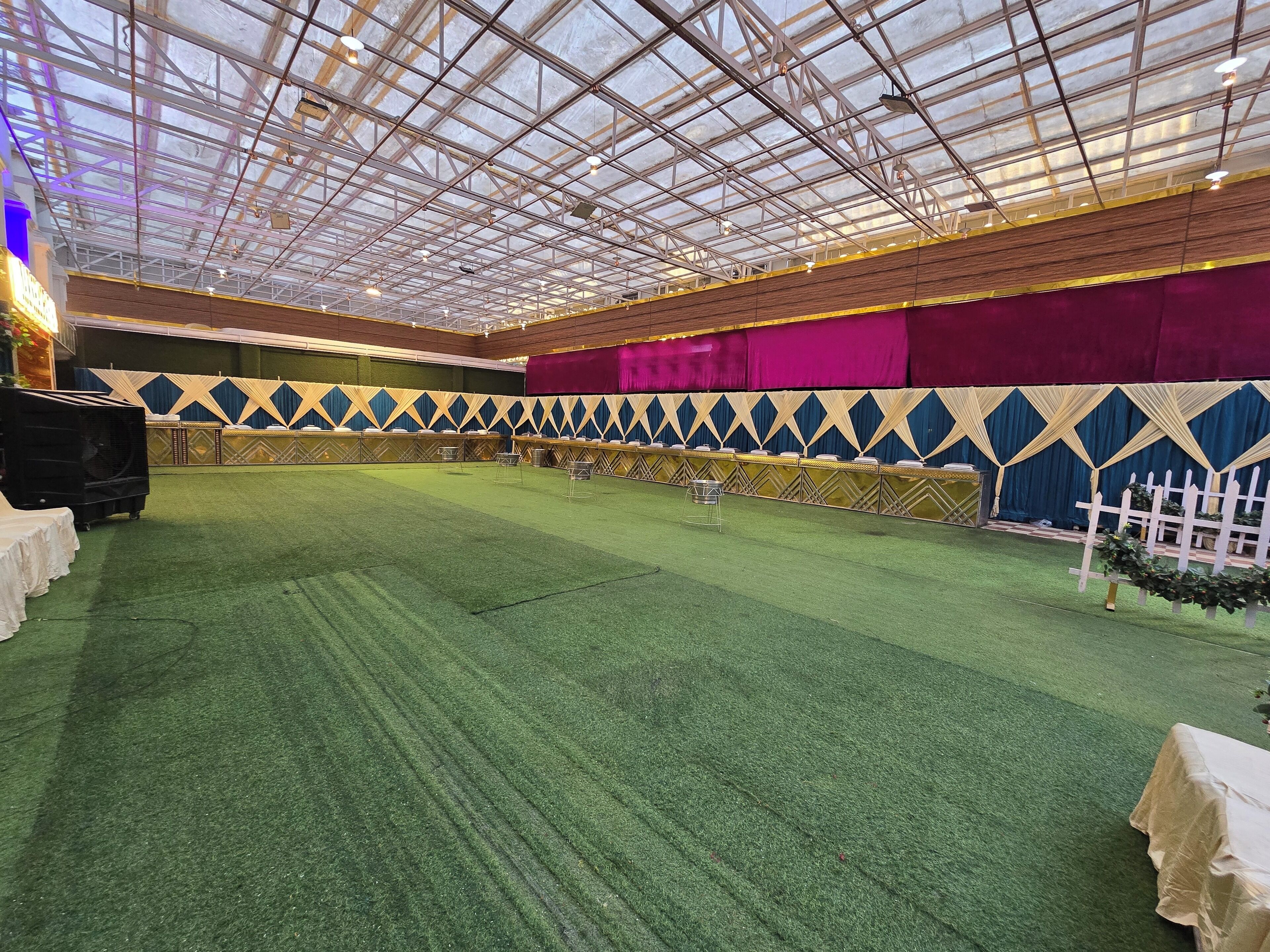 Un espacio interior con techo alto, suelo cubierto de moqueta verde y un área de escenario con un telón de fondo decorado.
