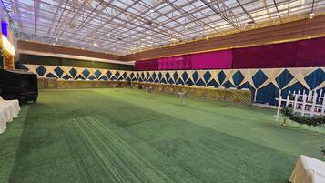 Un espacio interior con techo alto, suelo cubierto de moqueta verde y un área de escenario con un telón de fondo decorado.