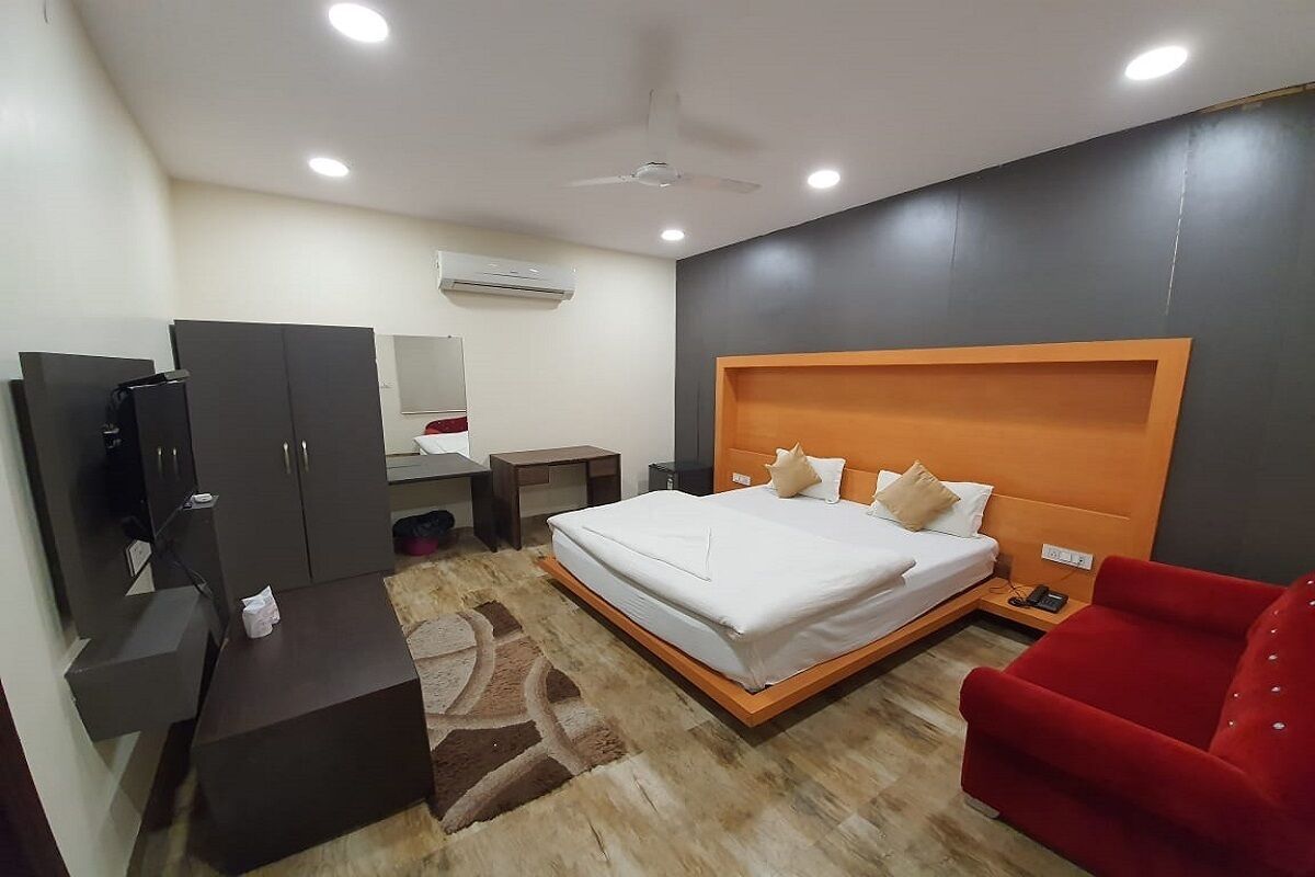 Une chambre d’hôtel moderne avec un grand lit, un fauteuil rouge, un bureau et une armoire.