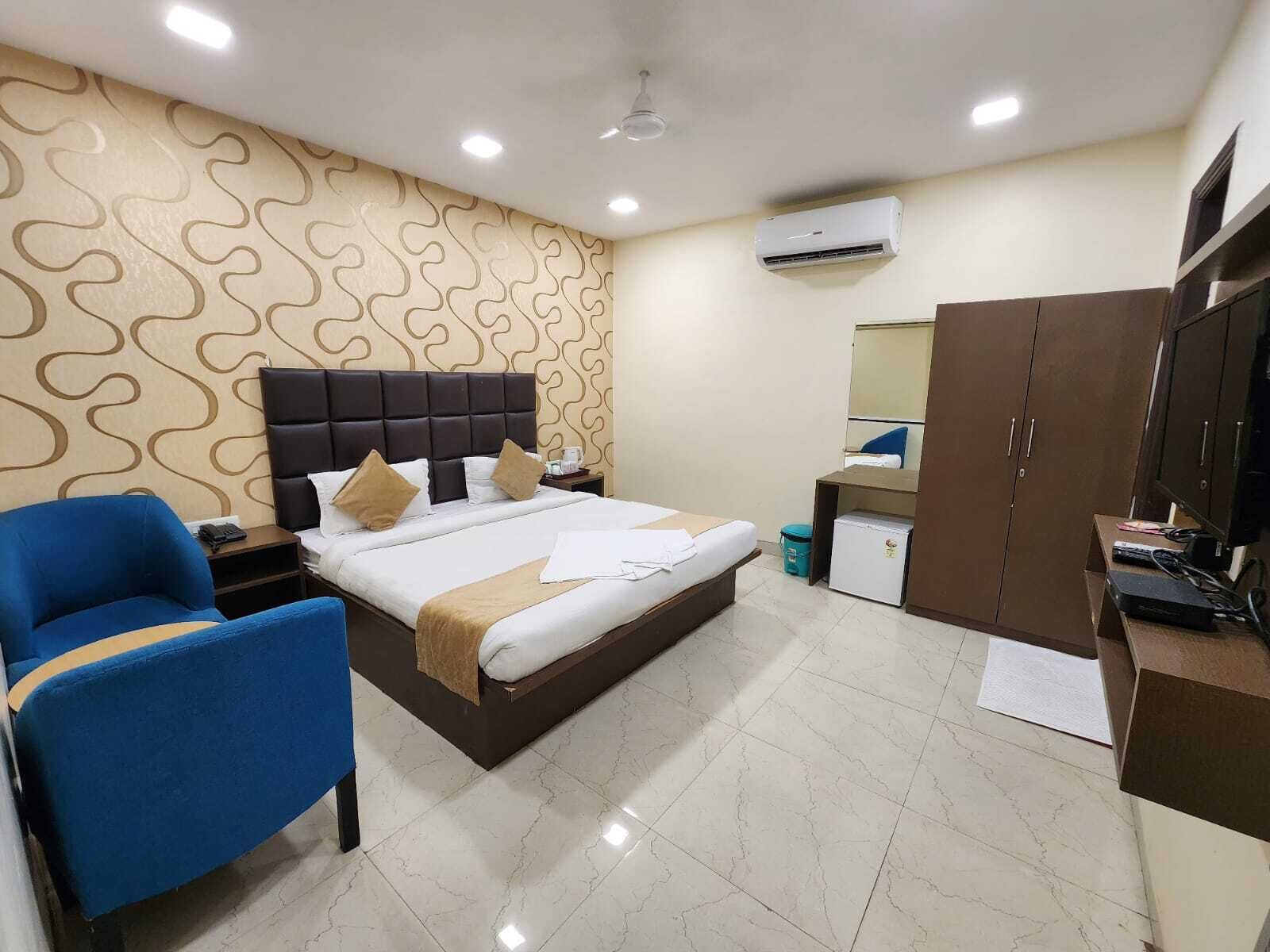 Une chambre d’hôtel comprenant un lit, une chaise bleue, une armoire, un bureau avec un ordinateur et un appareil de climatisation.