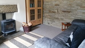 A cozy living room with a stone wall, a wooden cabinet, a fireplace, and a sofa. - Stunning cosy cottage! Close to Haworth and amenities (keighley)