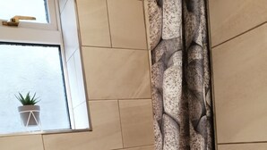 A bathroom with beige tiled walls, a window with a potted plant, and a shower curtain with a stone pattern. - Stunning cosy cottage! Close to Haworth and amenities (keighley)