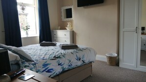 A bedroom with a bed, a dresser, a TV, and a window with curtains. - Stunning cosy cottage! Close to Haworth and amenities (keighley)