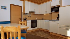 Une cuisine compacte avec des meubles blancs, un plafond en bois et un coin repas comprenant une table et des chaises.