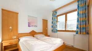 Un lit double avec une tête de lit en bois, une table de chevet, une commode, une fenêtre avec des rideaux et un radiateur.