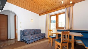 Une pièce chaleureuse avec un plafond en bois, un canapé bleu, une table à manger en bois avec des chaises, et une fenêtre avec des rideaux.