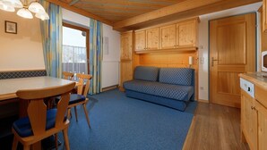 Una stanza accogliente con soffitto in legno, un tavolo da pranzo con sedie, un divano e un angolo cottura con pensili in legno.