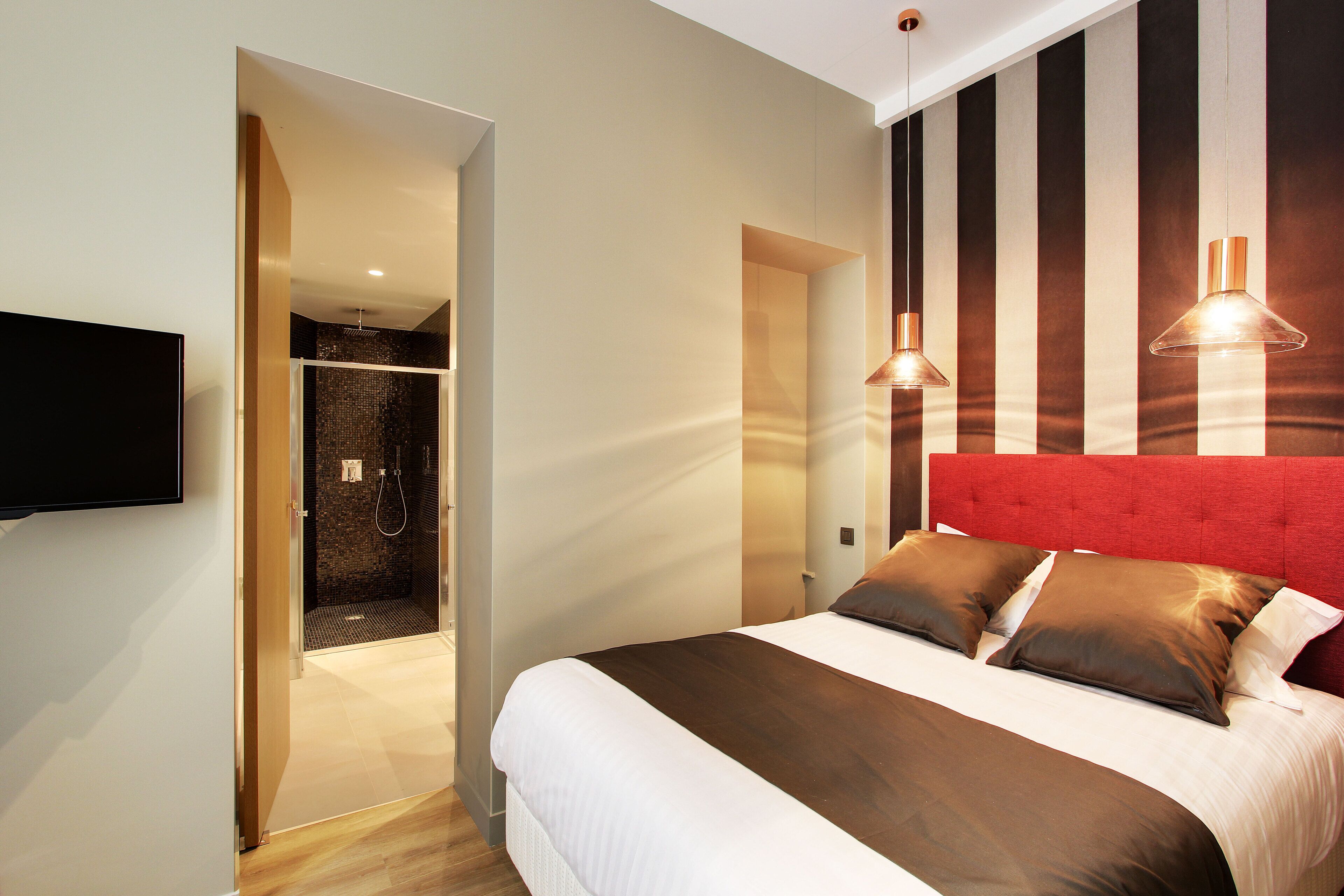 A modern hotel room with a large bed, a red headboard, and a television mounted on the wall.