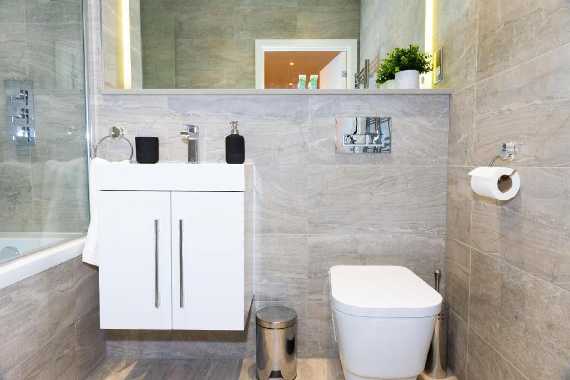 Ein modernes Badezimmer mit einem weißen Waschtisch, einer Toilette und einer kleinen Mülltonne.