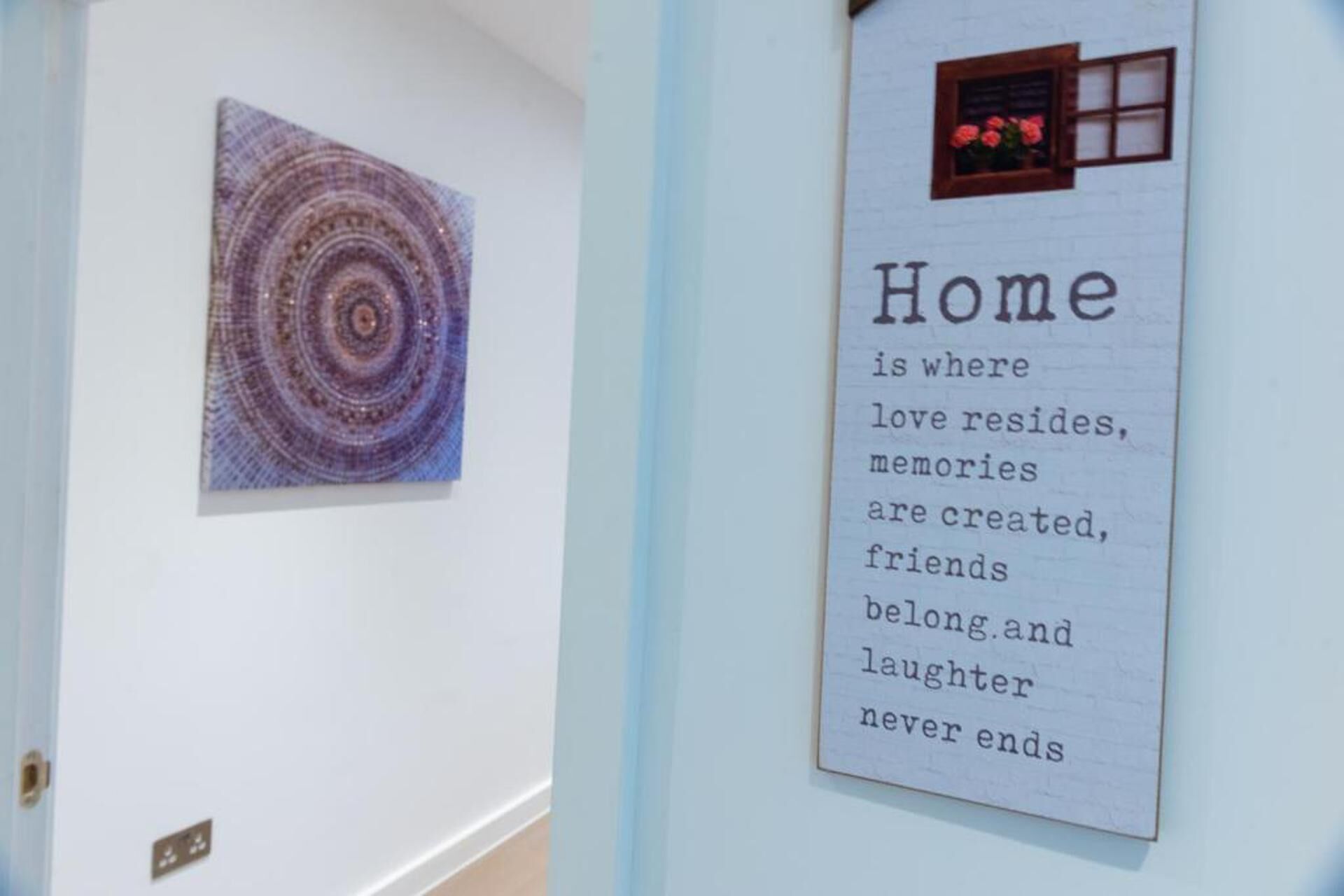 Una pared con una obra de arte circular y un texto enmarcado que dice: "El hogar es donde reside el amor, donde se crean recuerdos, donde los amigos son bienvenidos y donde la risa nunca termina."