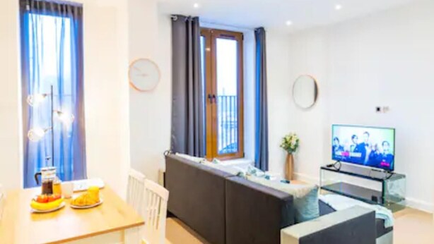 Un salon moderne comprenant un coin repas, un canapé, un téléviseur et une fenêtre avec des rideaux.