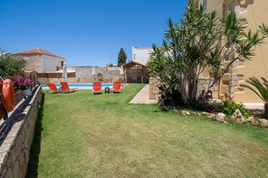 A backyard with a swimming pool, orange lounge chairs, and a stone wall.