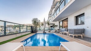 A rooftop pool with wooden deck, lounge chairs, and a view of the cityscape. - luxury garden apartment heated pool (Tiberias)
