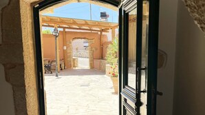 Une porte ouverte donne sur une cour intérieure agrémentée d’une pergola, de murs en pierre et de coins salons extérieurs.