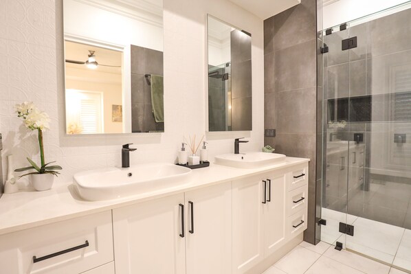 Un baño moderno con dos lavamanos, un espejo grande y una cabina de ducha de vidrio.