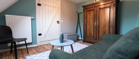 A room with a sloped ceiling, a wooden cabinet, a green sofa, a small round table, and a white radiator.