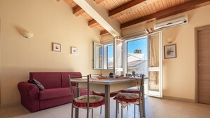 A cozy room with a red sofa, a dining table with chairs, and large windows offering a view of the outside. - Villa Tonnara 50m dal mare (Avola)