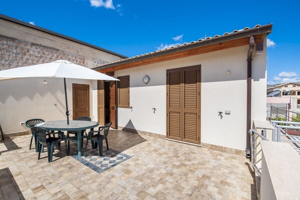 Un patio con una mesa y sillas, una sombrilla blanca y contraventanas de madera en un edificio.