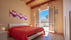 A bedroom with a bed, a nightstand, a lamp, and a sliding glass door leading to an outdoor area. - Villa Tonnara 50m dal mare (Avola)