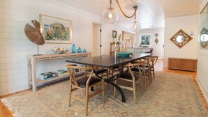 Un espace repas avec une longue table, des chaises en bois et un tapis à motifs.