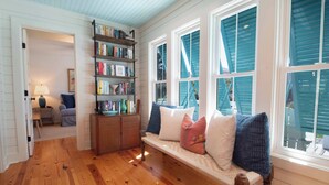 Une pièce chaleureuse avec un plancher en bois, un banc agrémenté de coussins, une bibliothèque et une fenêtre avec des volets.