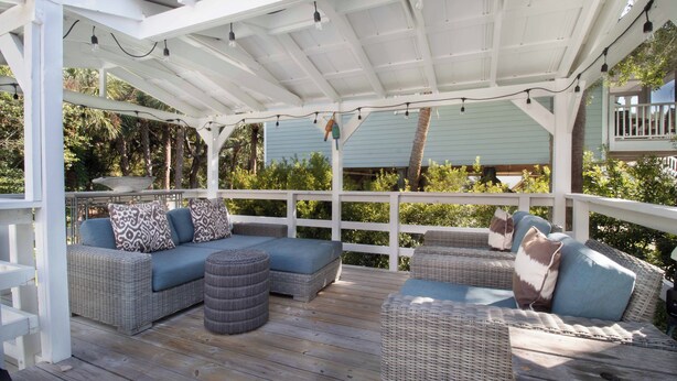 Un espace extérieur abrité, aménagé avec des meubles en osier et des coussins, une terrasse en bois et une rambarde blanche.
