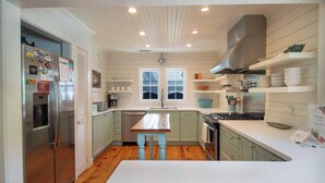 Une cuisine moderne avec des meubles blancs, un banc en bois et un réfrigérateur en acier inoxydable.