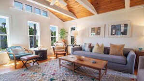 Un salon chaleureux avec un plafond en bois, un canapé gris, un fauteuil bleu et un tapis à motifs.