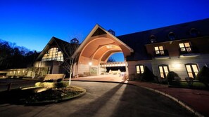 A hotel with a prominent arched entrance, a well-lit driveway, and a landscaped front yard.