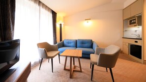 A compact living space with a sofa, two armchairs, a coffee table, a television, and a kitchenette.