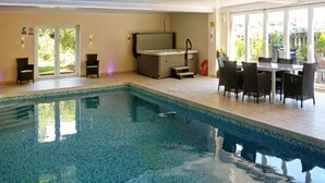 Ein Hallenbad mit Whirlpool, einem Tisch mit Stühlen und Blick auf Grünflächen.