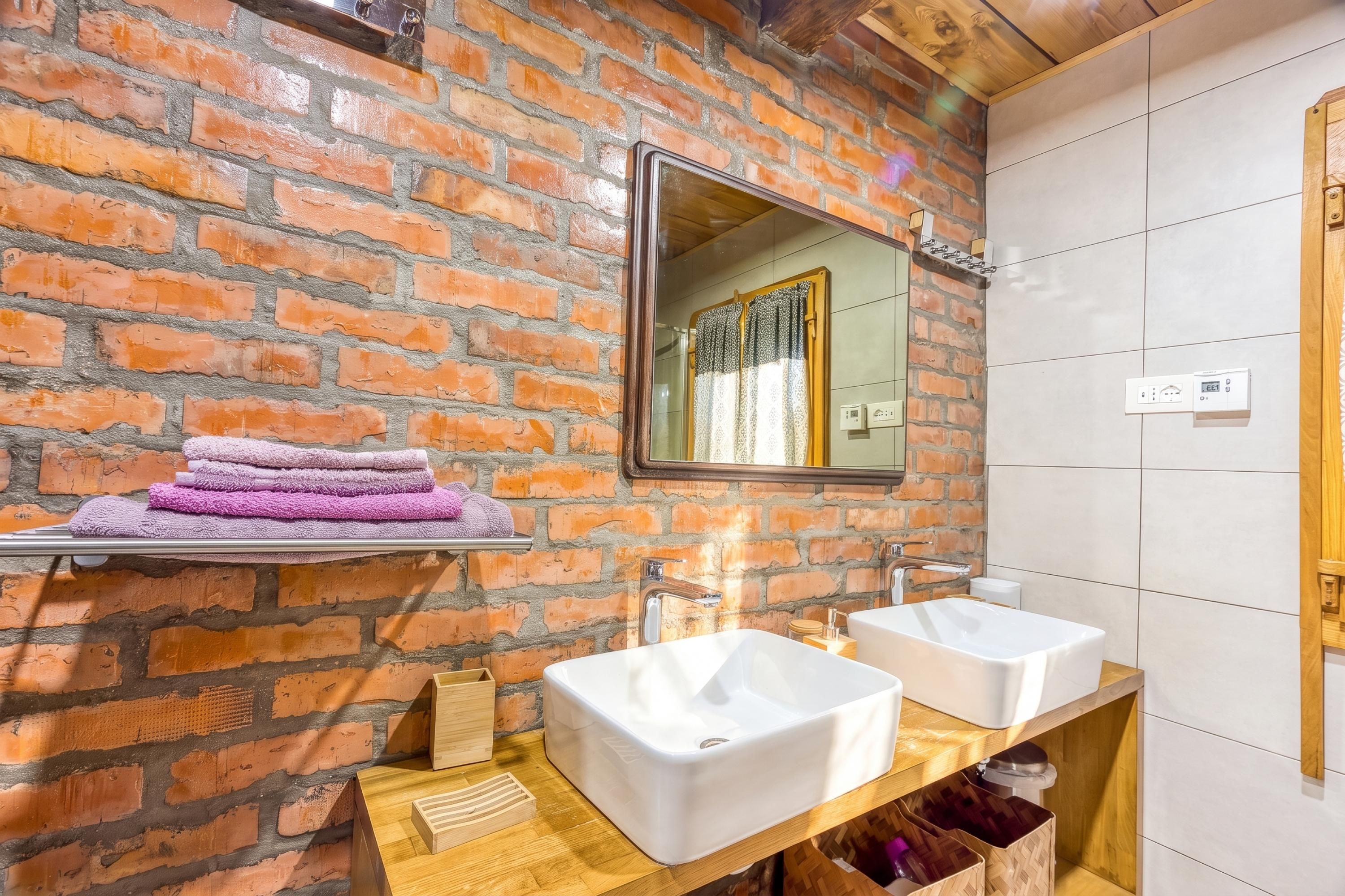 A bathroom with a brick wall, two sinks, a mirror, and a towel rack with folded towels.