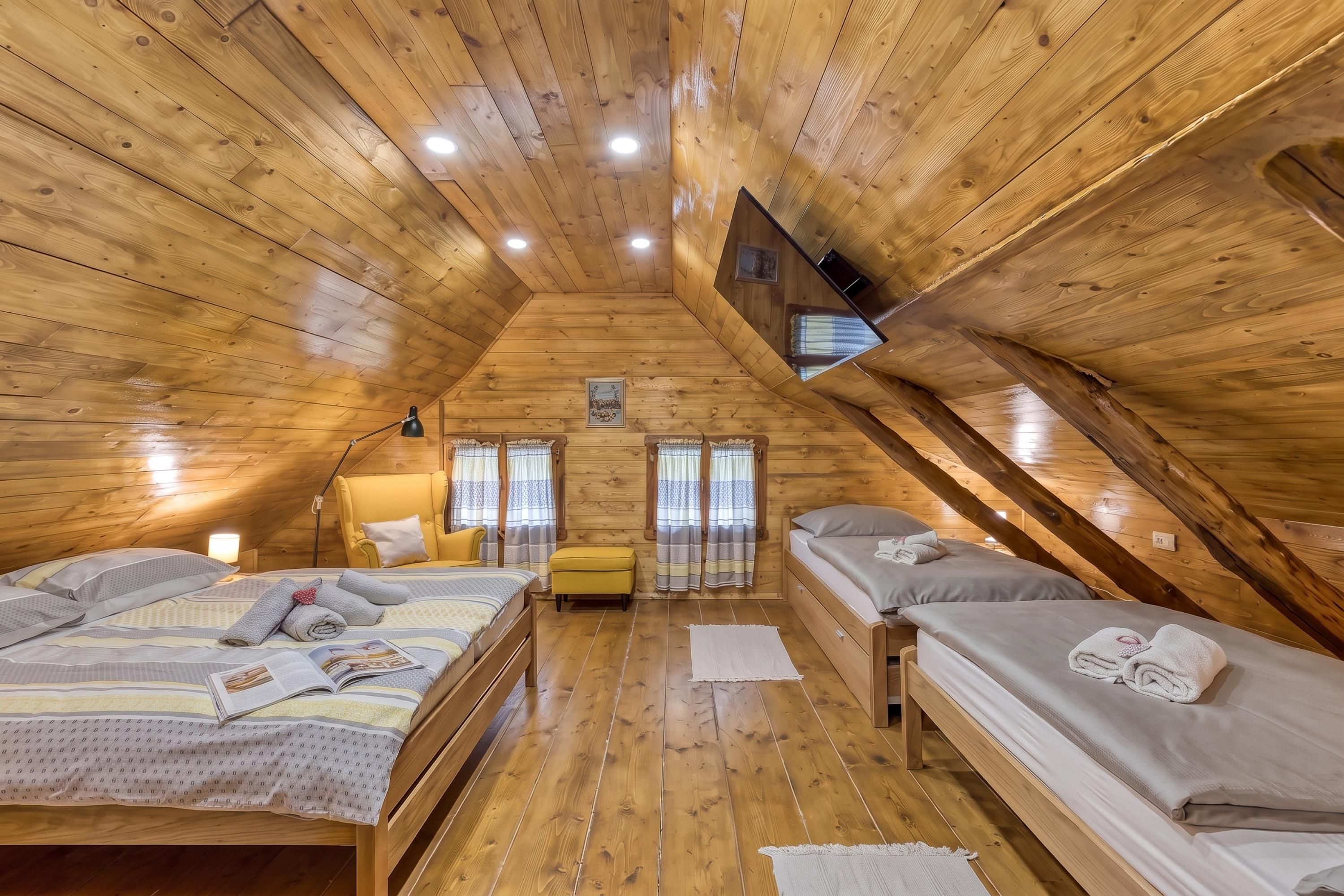 A cozy attic bedroom with wooden walls and a sloped ceiling, featuring two beds, a chair, and a small table.