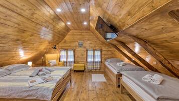 A cozy attic bedroom with wooden walls and a sloped ceiling, featuring two beds, a chair, and a small table.