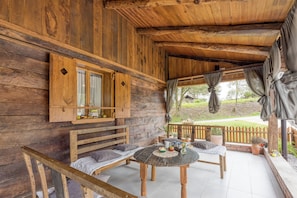 Une cabane en bois dotée d’un porche, aménagée avec une table ronde, des chaises et un banc.