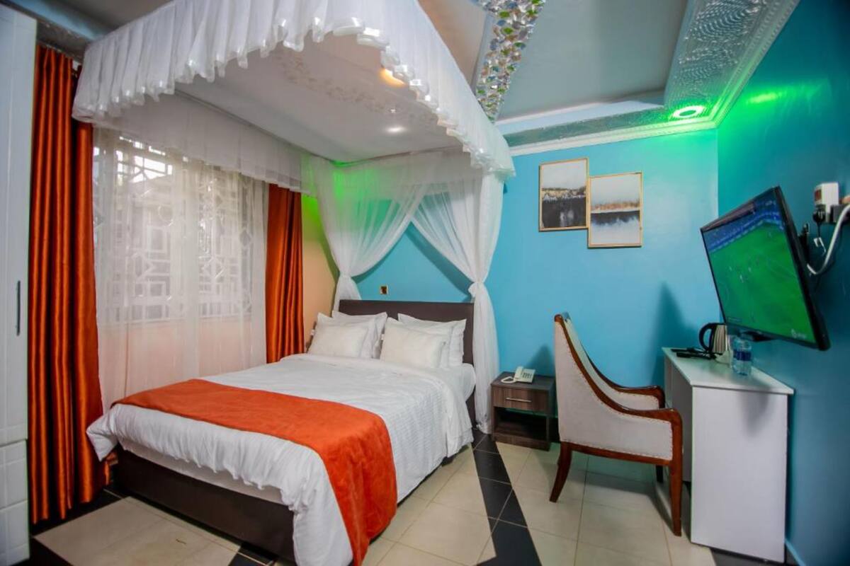 Habitación de hotel con cama, escritorio, silla, televisor y ventana con cortinas.