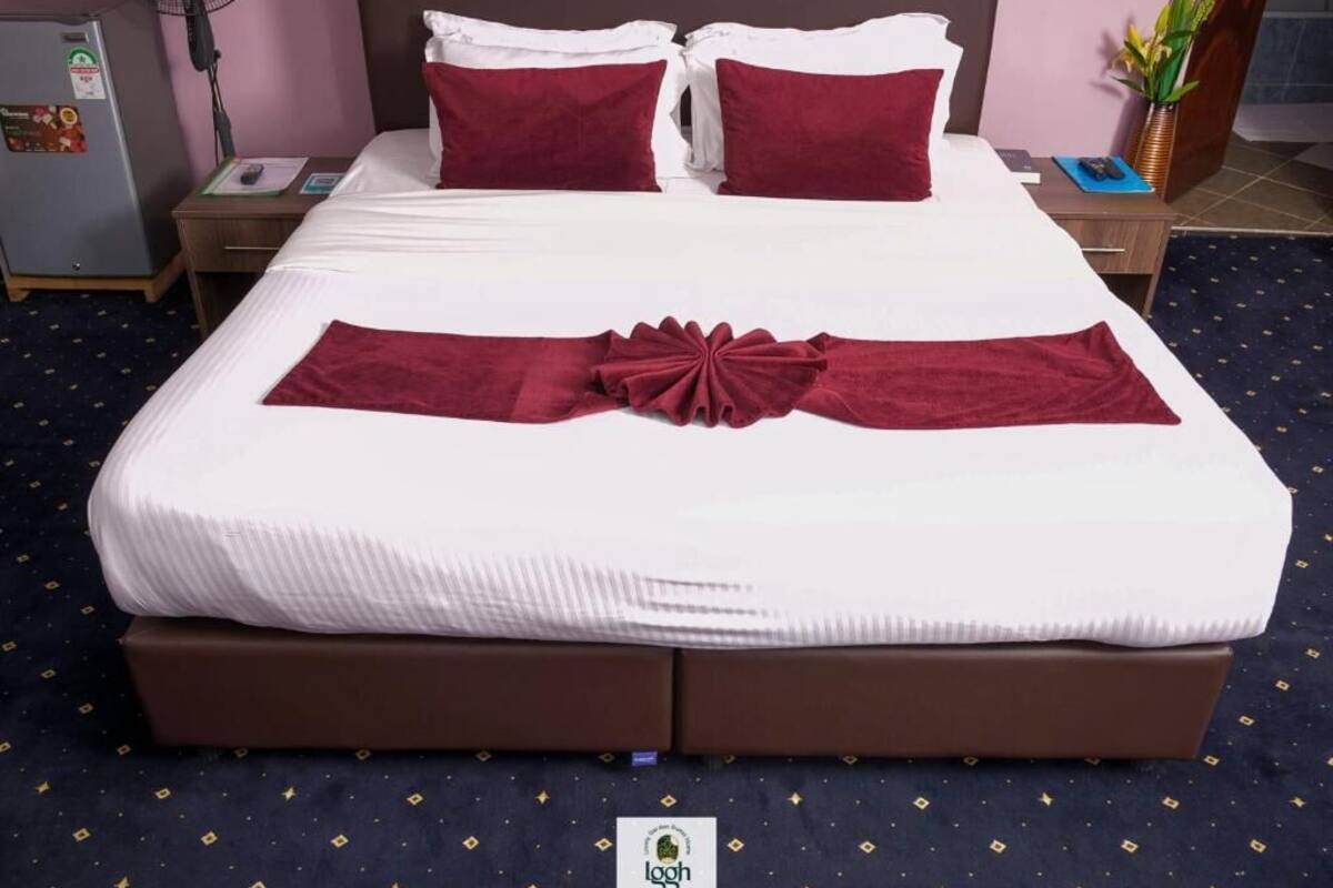 Una cama bien tendida con una colcha blanca y roja, un lazo decorativo rojo y un logotipo en el lateral de la cama.